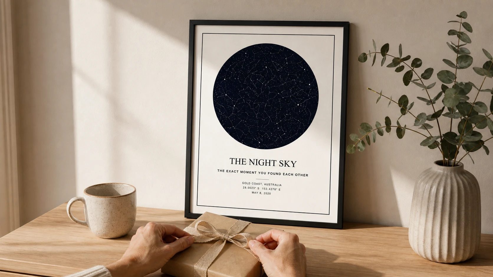 Faceless hands wrapping a Father's Day gift beside a framed navy star map in a warm neutral home